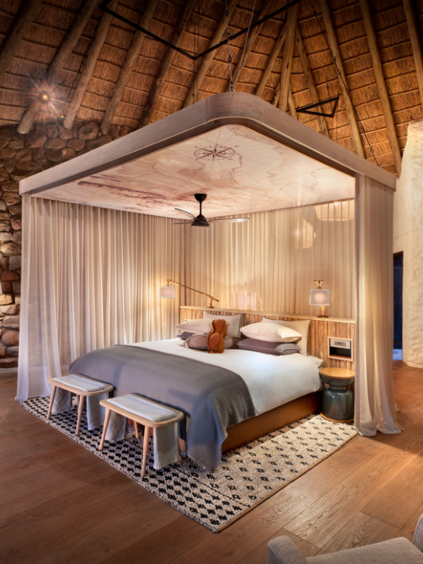 The interior of a luxury safari suite featuring a large bed positioned under a massive, suspended wooden canopy with an antique map printed on the ceiling